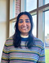 Postdoctoral Fellow Maleeha Naqvi wearing a striped colorful sweater smiling at the camera